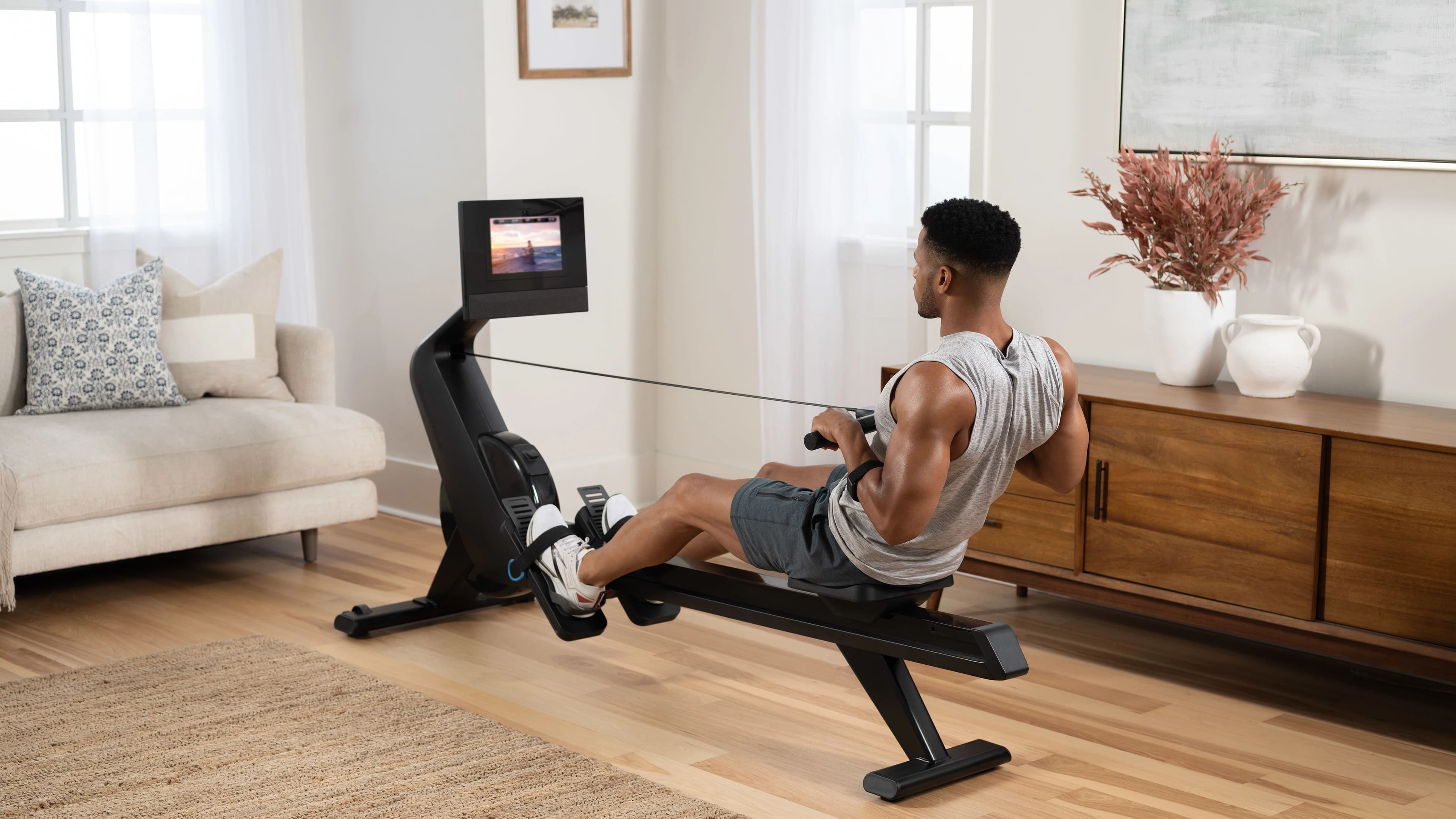 NordicTrack RW700 rowing machine in a home gym setting with iFIT scenic workout streaming on the 10-inch touchscreen, showing connected rowing at home