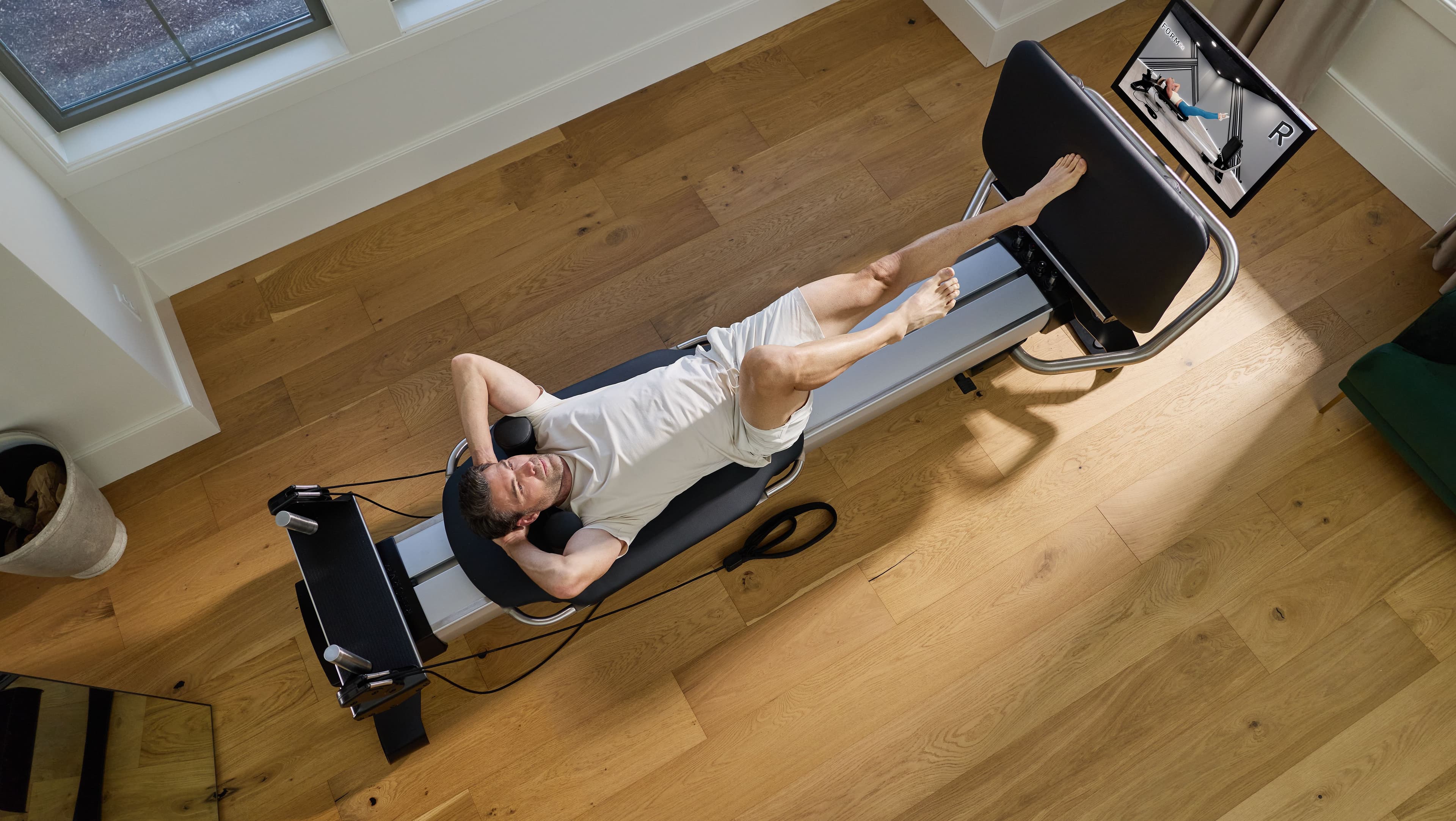 Overhead view of a resident following a guided iFIT session on the NordicTrack Ultra 1 Reform RX-S in a light-filled home studio. The connected reformer luxury apartment buildings are adding to amenity floors for self-directed resident use without a dedicated instructor on shift.
