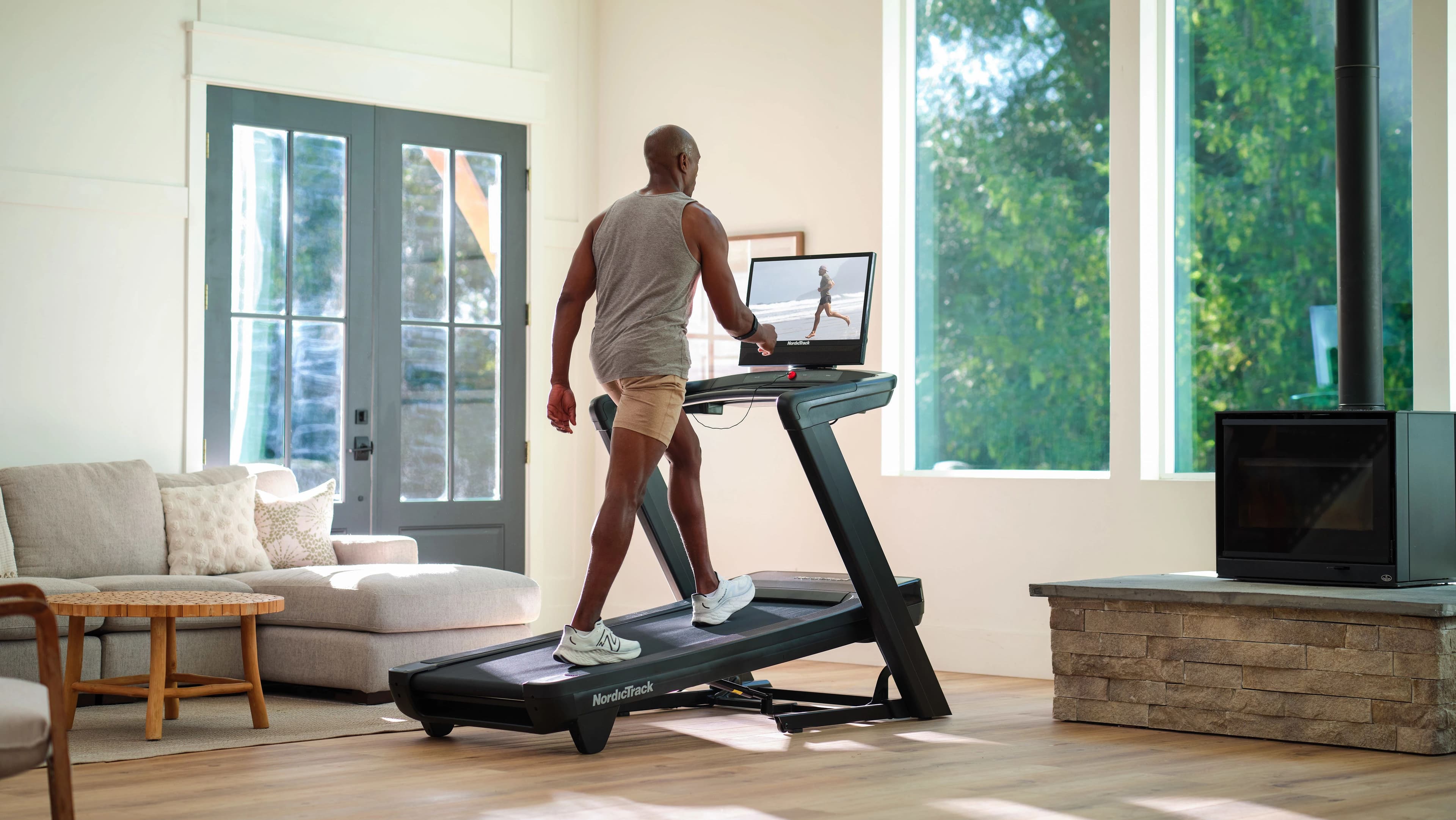 A man walks on a NordicTrack 2450 treadmill in a sunny home living room, following an iFIT trainer-led session — showing how connected walking fits naturally into daily life.